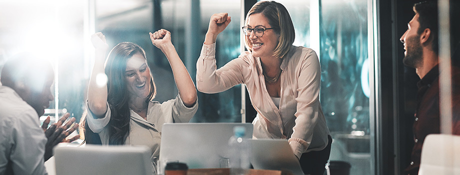 Humanitarian careers allow you to effect change and better people’s lives. Woman meeting with coworkers in a nonprofit setting raises her hands in celebration.